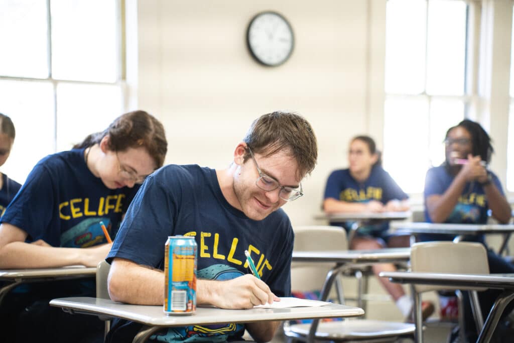 a student smiling as he is writing in his notebook.