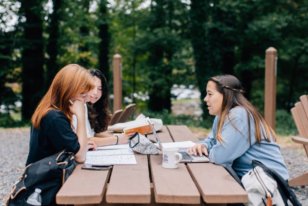 students having a discussion on a picnic table by the pond.