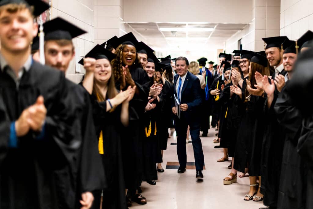 Graduating Toccoa Falls College students line a hallway as a professor walks between them
