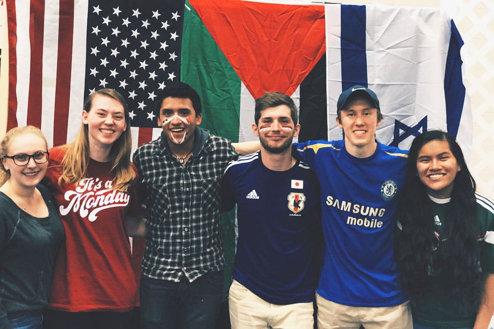 Young people standing arm in arm in front of various country flags