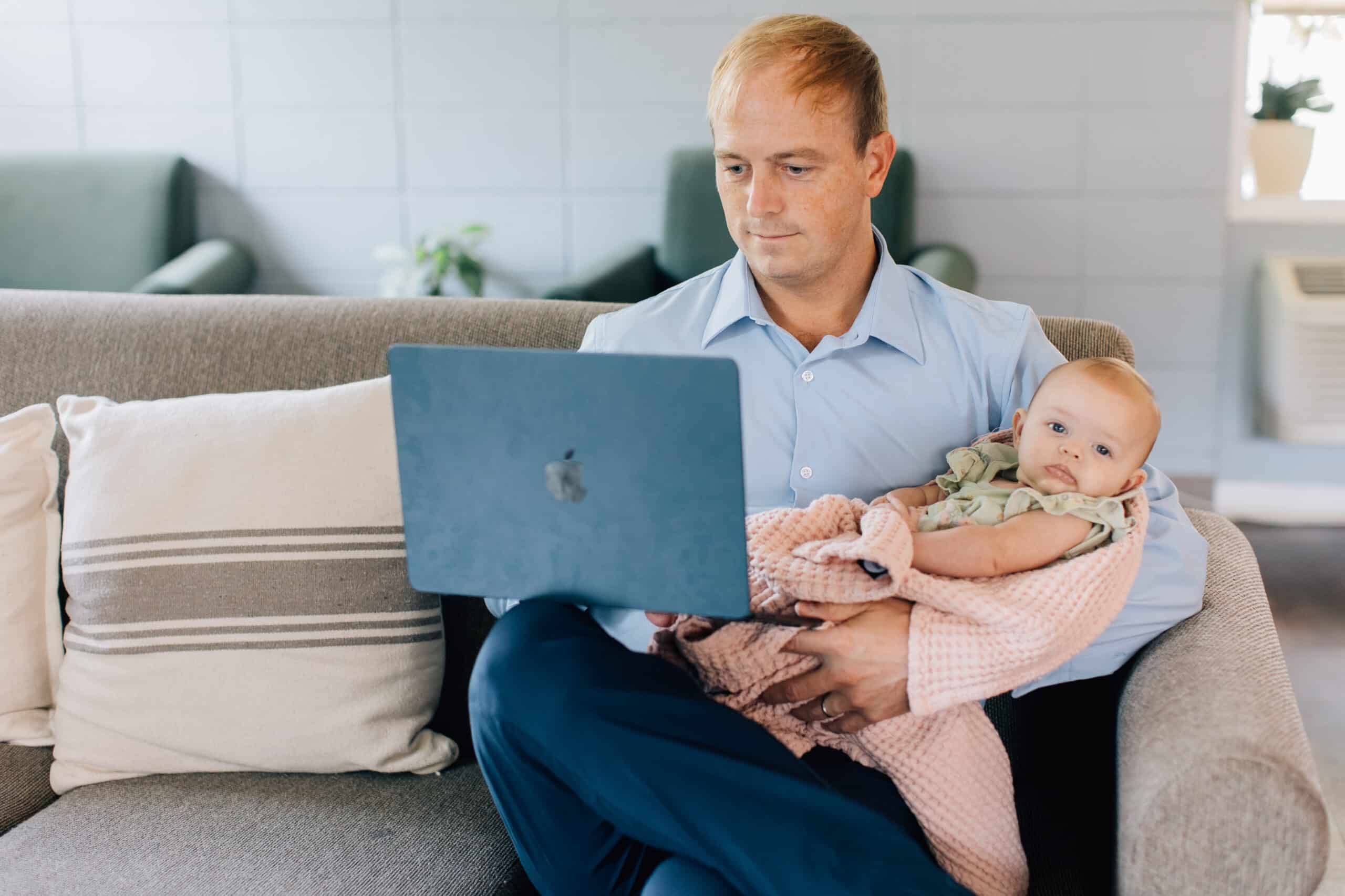 Student working on laptop with a baby in his arms.